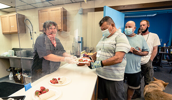 Photo of a volunteer serving a meal to several men at the Kelly Shelter
